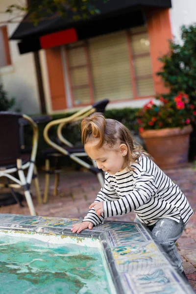 stock image toddler girl in striped long sleeve shirt looking at water in fountain on street in Miami 