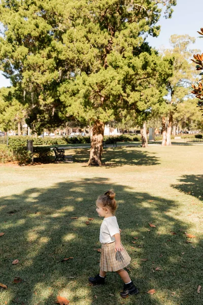 stock image joyful baby girl in white t-shirt and skirt playing in green park 