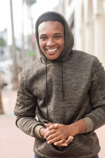 Stock image overjoyed african american man in hooded sweatshirt looking at camera while smiling outdoors 