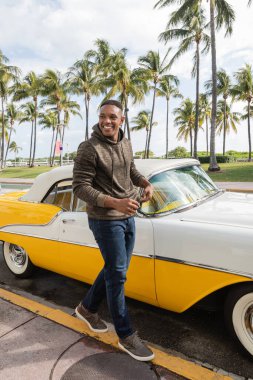 MIAMI, FLORIDA, ABD - 15 Aralık 2022: Klasik retro arabanın yanında yürüyen mutlu Afrikalı Amerikalı adam 