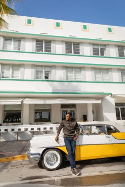 MIAMI, FLORIDA, ABD - 15 ARALIK 2022: Mutlu Afrikalı Amerikalı adam retro arabanın yanında duruyor 