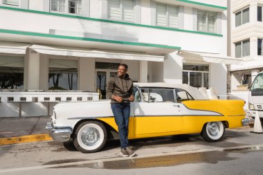 MIAMI, FLORIDA, ABD - 15 Aralık 2022: neşeli Afrikalı Amerikalı adam klasik retro arabanın yanında duruyor 