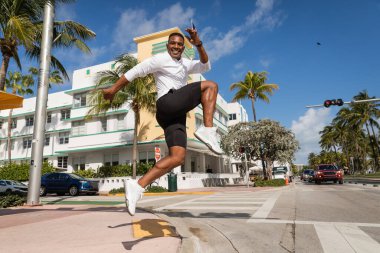 Miami 'de palmiye ağaçlarının ve modern apartmanın yanına atlayan neşeli Afro-Amerikan adam. 