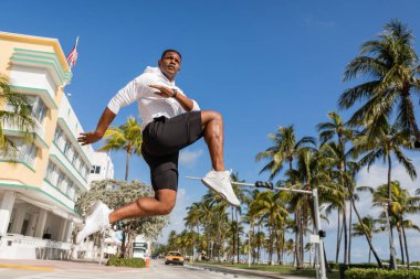 Sportif Afro-Amerikan adam Miami 'de palmiye ağaçlarının ve modern apartmanın yanına atlıyor. 