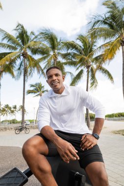 Miami 'de spor salonunda çapraz antrenör ekipmanının üzerinde oturan neşeli Afro-Amerikan adam.