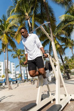 Miami 'deki palmiye ağaçlarının yanındaki spor salonunda çalışan Afro-Amerikan sporcunun tam boy görüntüsü. 