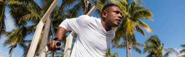 Miami plajında çalışan Afrikalı Amerikan sporcusunun düşük açılı görüntüsü, afiş. 