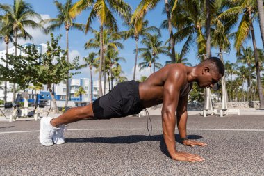Üstsüz Afro-Amerikan sporcusu Miami sahilinde palmiye ağaçlarının yanında tahta egzersizi yapıyor. 
