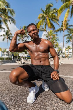 Şortlu ve spor ayakkabılı güçlü Afro-Amerikan sporcusu Miami plajındaki antrenmandan sonra kaslarını gösteriyor. 