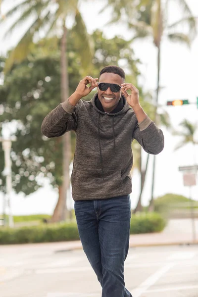 stock image happy african american man in hoodie and jeans wearing sunglasses on street in Miami 