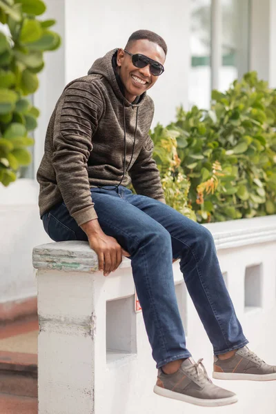 stock image full length of cheerful african american man in hoodie and sunglasses sitting on street in Miami 