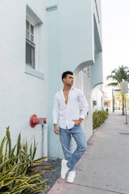 Miami 'de sokakta poz veren şık gömlekli ve kot pantolonlu uzun kıvırcık Kübalı bir adam.