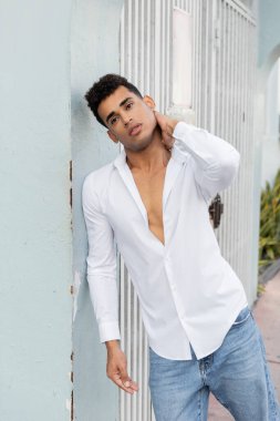 Beyaz gömlekli ve kot pantolonlu şık Kübalı adam Miami 'de bir binanın yanında dikilirken boyuna dokunuyor.