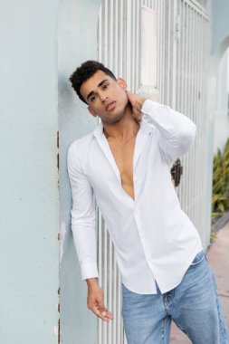 Beyaz gömlekli ve kot pantolonlu şık Kübalı adam Miami 'de bir binanın yanında dikilirken boyuna dokunuyor.