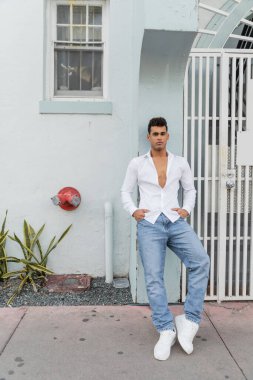 Tişörtlü ve kot pantolonlu modaya uygun Kübalı adam Miami 'de kapısı olan binanın yanında duruyor.