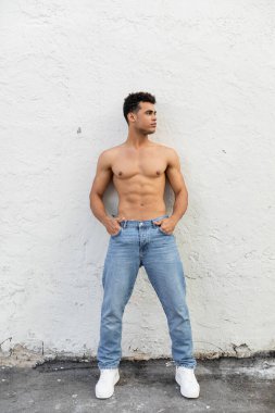 Miami 'de tatil sırasında beyaz bina duvarının yanında poz veren kot pantolonlu seksi kaslı genç Kübalı adam.