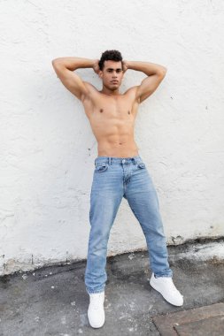 Full length of athletic cuban man in blue jeans posing near building on  street in Miami clipart