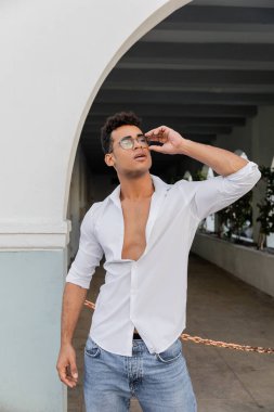 Miami 'de beyaz gömlekli ve kot pantolonlu seksi genç adam yuvarlak gözlüklere dokunuyor.
