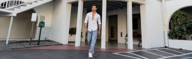 Gözlüklü, kot pantolonlu ve beyaz gömlekli genç ve modaya uygun Kübalı adam binanın yanında yürüyor. 