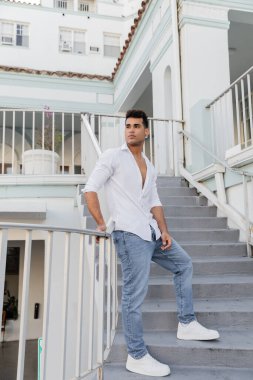 Miami 'de merdivenlerde duran beyaz gömlekli ve kot pantolonlu şık Kübalı bir adam.