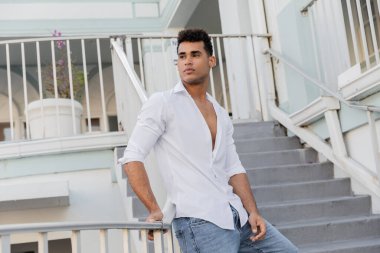 Beyaz gömlekli ve kotlu yakışıklı Kübalı adam Miami 'de korkulukların yanında dikilirken gözlerini kaçırıyor.