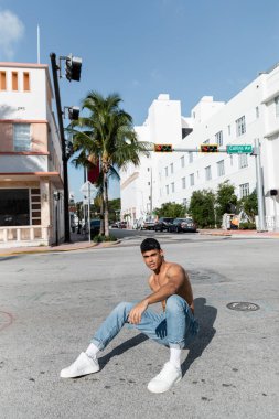 Beyzbol şapkalı ve kot pantolonlu yakışıklı Kübalı Miami 'de yolda oturuyor. 