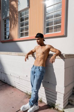 Beyzbol şapkalı ve kot pantolonlu seksi, üstsüz Kübalı adam Miami caddesinde duruyor.