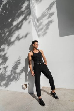 Miami 'de, güney sahilinde, şehir sokağında gölgeli beyaz duvarın yanında poz veren seksi Kübalı genç adam.