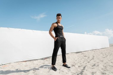 Siyah elbiseli kaslı genç Kübalı adam Miami 'de, güney sahilinde elleri ceplerinde poz veriyor.