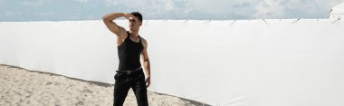 Siyah kıyafetli, kaslı Kübalı adam Miami 'de, güney sahilinde, pankartta yüzünü kapatıyor. 