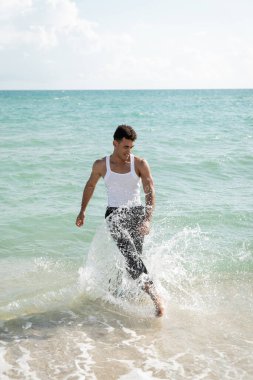 Gülümseyen ve kaslı Kübalı genç adam Miami South Beach 'te okyanus suyunda dikilirken eğleniyor.