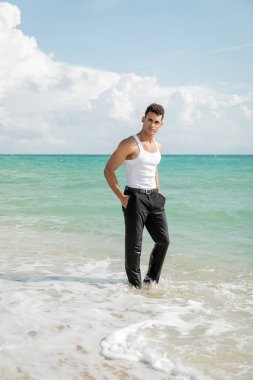 Miami Güney Sahili 'nde okyanus suyunda elleri ceplerinde duran kaslı genç Kübalı adam.