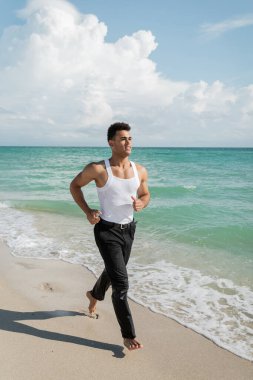 Mutlu Kübalı genç adam Miami South Beach, Florida 'nın okyanus suyunun yanında kumların üzerinde koşuyor.