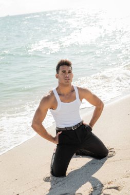Yakışıklı ve kaslı Kübalı adam Miami South Beach 'te okyanus kenarında poz veriyor ve kameraya bakıyor.