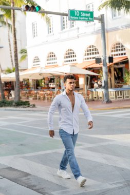 Miami 'de, güney sahilinde şehir sokağında yürüyen gömlek ve kot pantolonlu genç Kübalı adam.
