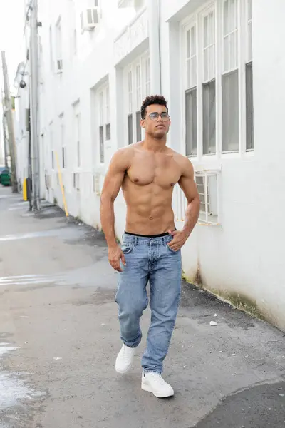 stock image sexy cuban man in round-shaped eyeglasses and jeans looking away while walking in Miami