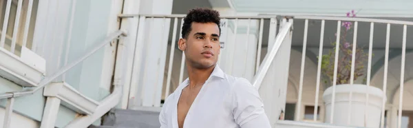 stock image cuban man with curly hair and in white shirt looking away on urban street in Miami, banner 