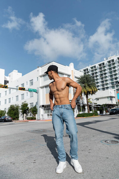 sexy young cuban man in jeans and baseball cap walking on urban street in Miam, summer 