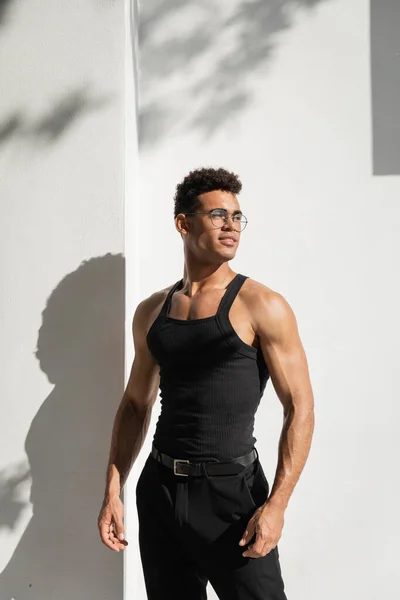 stock image Stylish and cheerful young cuban man in eyeglasses near building with shadow on street in Miami