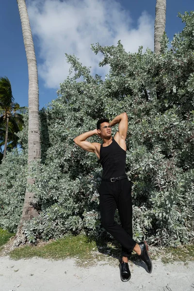 stock image muscular cuban man in black outfit and eyeglasses near green plants outdoors in Miami, south beach