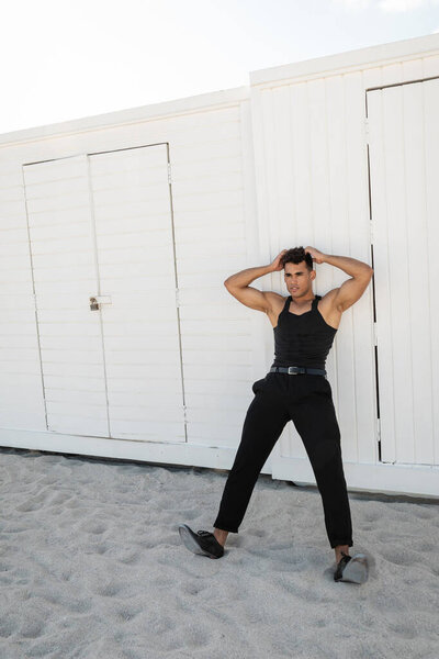 Relaxed and muscular young cuban man in black outfit touching head in Miami, south beach