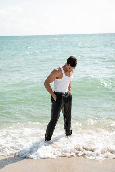 cuban man in wet clothes holding hands in pockets while standing in ocean water in Miami South Beach