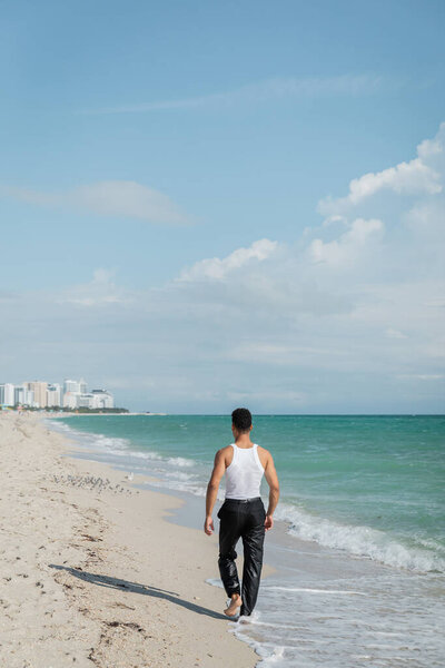 Back view of young man walking on sand near ocean water of Miami South Beach, Florida