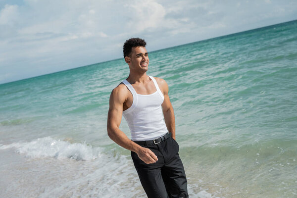 Muscular cuban young man standing on sand near ocean water of Miami South Beach, Florida