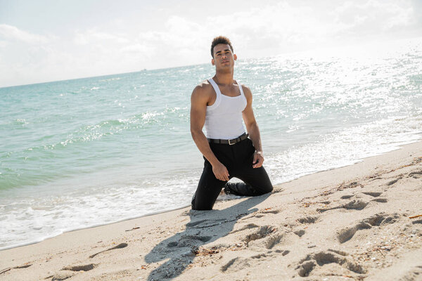 young cuban man in stylish clothes posing on coast sand near ocean and in Miami South Beach, Florida
