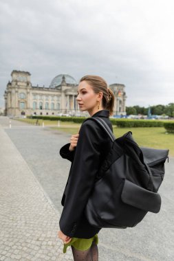 Berlin 'de Reichstag Binası' nın yakınlarında yürürken ceketli ve elbiseli bir kız.