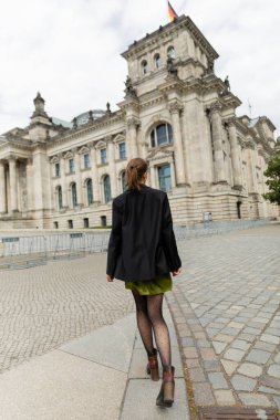 Berlin 'deki Reichstag Binası' nın yakınlarında, ceketli ve elbiseli şık bir kadının arka plan görüntüsü.