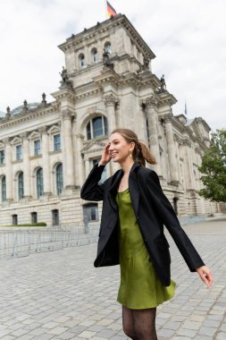 Ceketli ve ipek elbiseli neşeli ve şık genç bir kadın Reichstag Binası 'nın yakınlarına bakıyor.