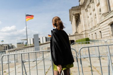 Açık renk saçlı, ceketli ve elbisesi olan bir kadın Reichstag Binası 'nın yanında dikiliyor. 