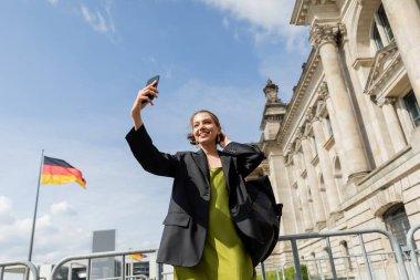 Sırt çantalı mutlu kadın Almanya, Berlin 'deki Reichstag Binası yakınlarında selfie çekiyor. 